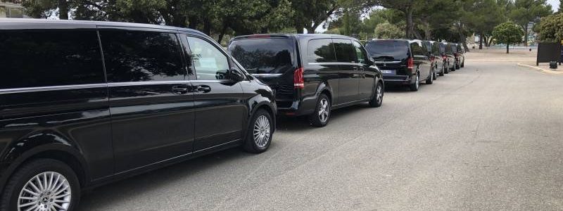Plusieurs véhicules noirs alignés sur une route pour le transport de groupes
